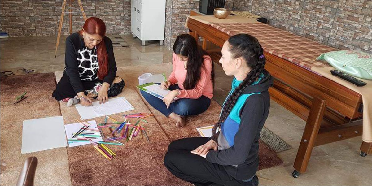 An art therapy session at SFCT: participants seated on the floor colouring mandala-style drawings with a practitioner.