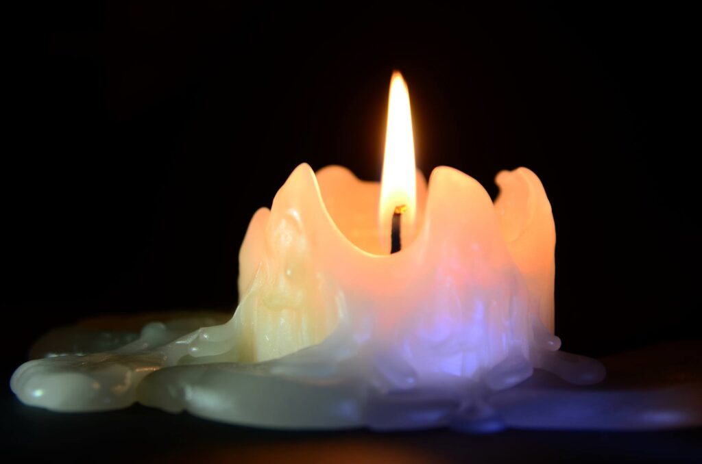 A lit candle burning low, with wax melting and pooling around its base
