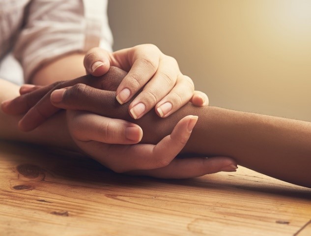 Close-up of two people's hands clasped together in comfort on a wooden table