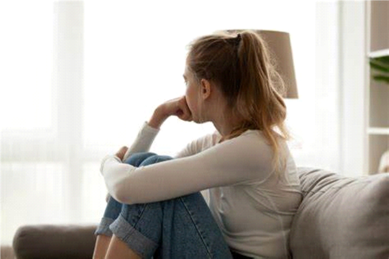 A young woman sitting on a sofa, resting her chin on her hand and looking away thoughtfully