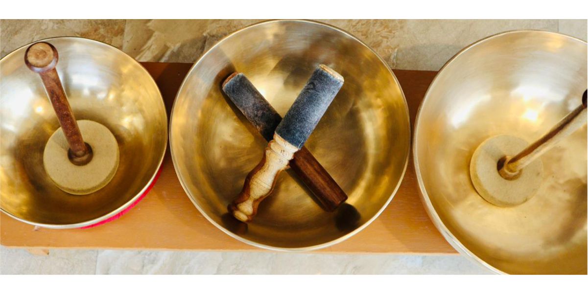 Three brass Tibetan singing bowls with wooden mallets resting inside, arranged in a row, used in sound healing therapy.